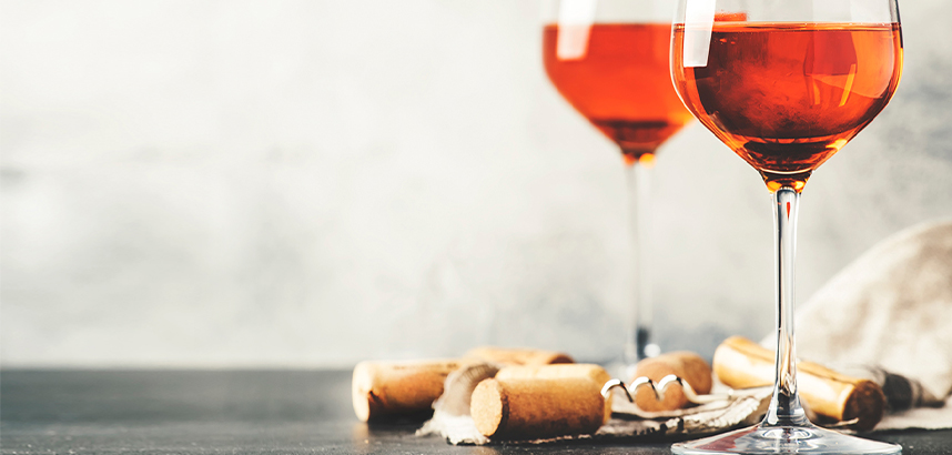 Zwei Gläser roséfarbenen Weins stehen neben Korken und Korkenzieher auf dunklem Tisch.