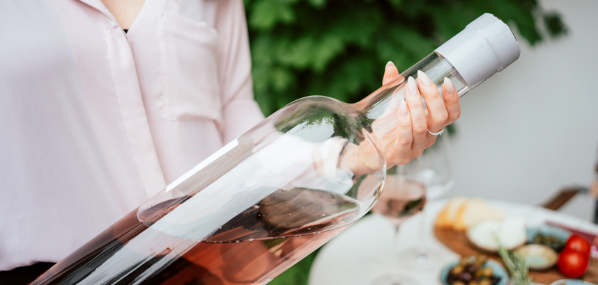 Person hält grosse Flasche Roséwein, Tisch mit Gläsern und Snacks.
