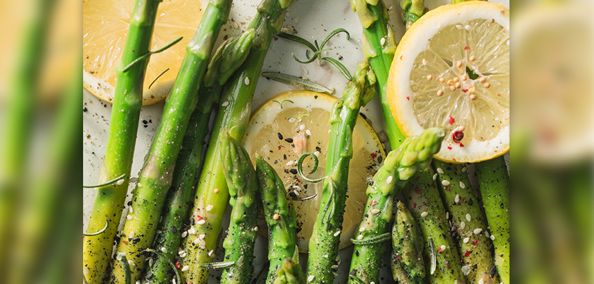 Grüner Spargel mit Zitronenscheiben, Gewürzen und Kräutern garniert.