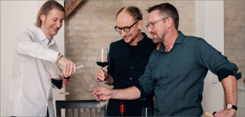 VINOS-Weinentdecker stossen mit Weingläsern an, lächeln und unterhalten sich.